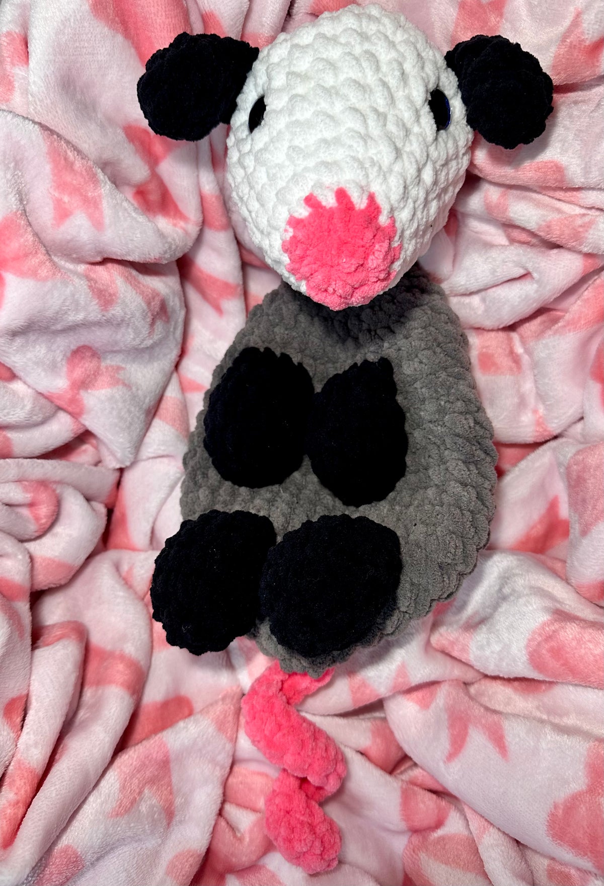 Handmade crochet opossum snuggler with white head, gray body, black ears and hands, pink nose and tail
